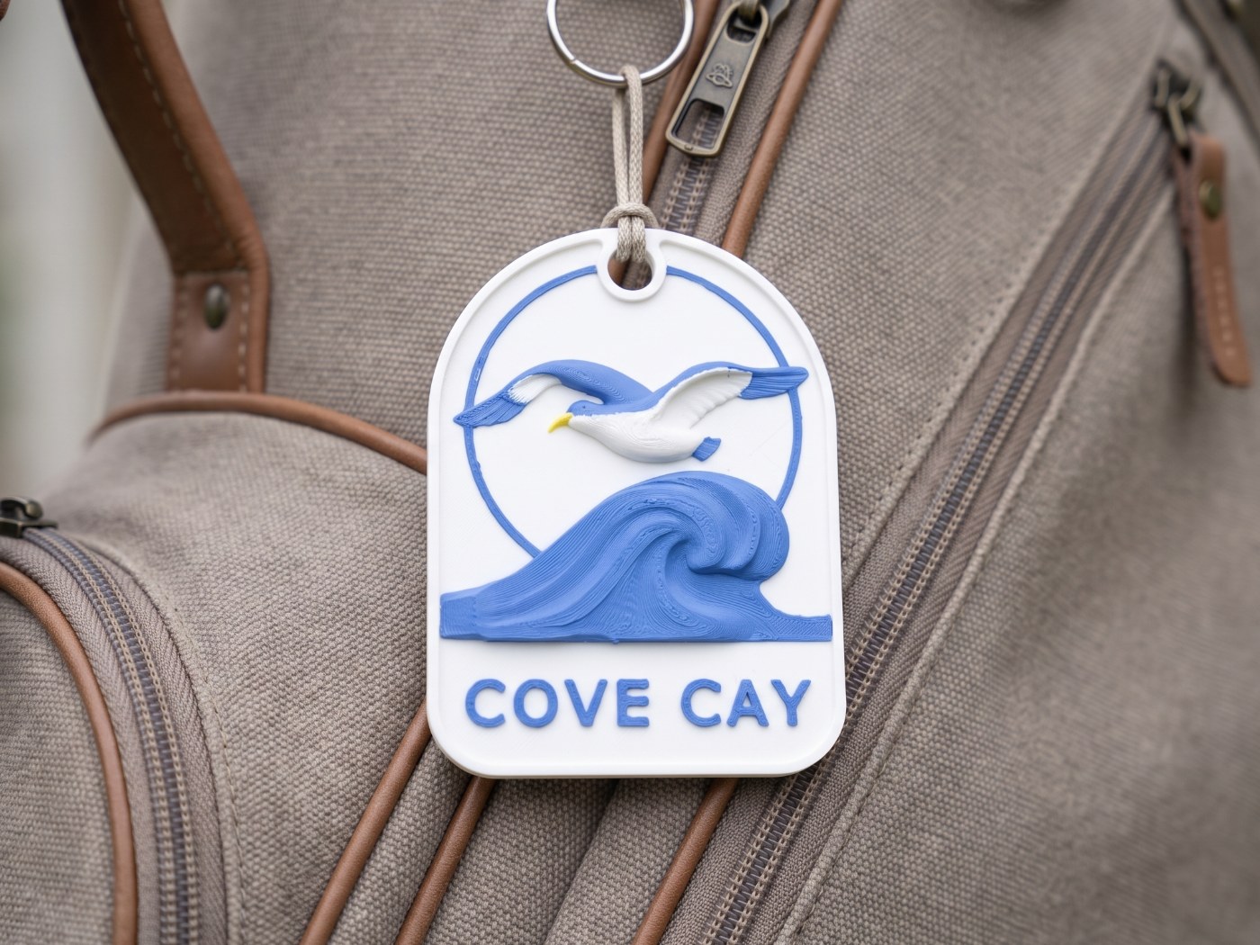 White arched Cove Cay bag tag with a seagull over a blue wave, hung on a canvas golf bag