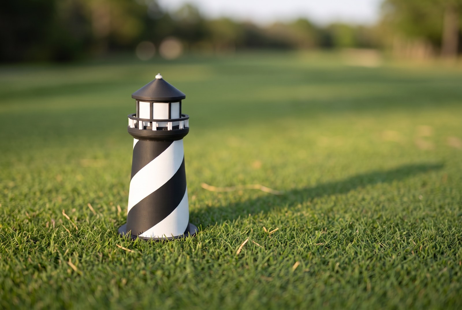 Heritage Harbour marker — sculpted black-and-white spiral-striped lighthouse with a railed gallery, set on a fairway at golden hour