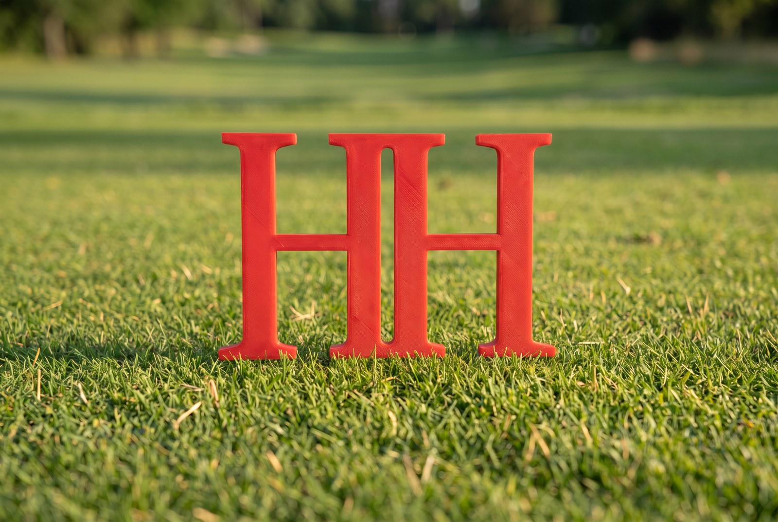 Heritage Harbour marker — red serif double-H monogram standing in fairway grass at golden hour