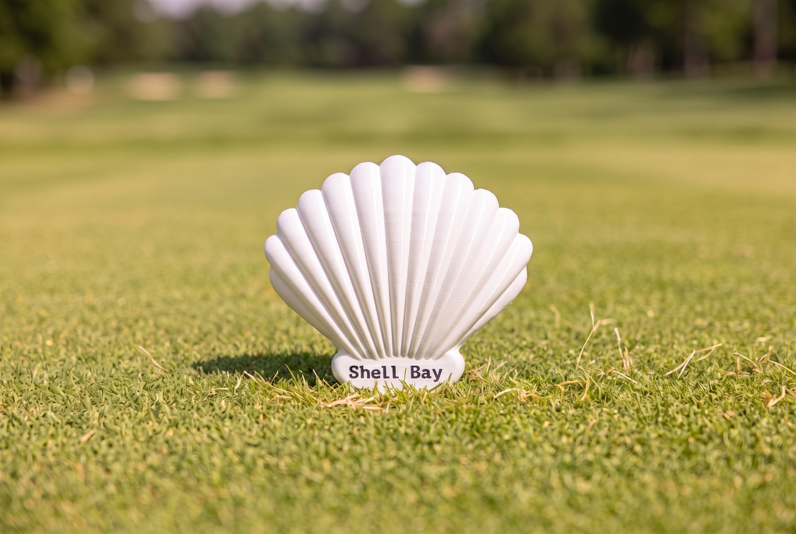Shell Bay marker — white fan-shell with ribbed relief and the course name embossed at the base, set on a green